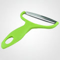 A bright green handheld vegetable peeler with a stainless steel blade, shown on a white background with tomatoes, basil, and garlic at the bottom right.