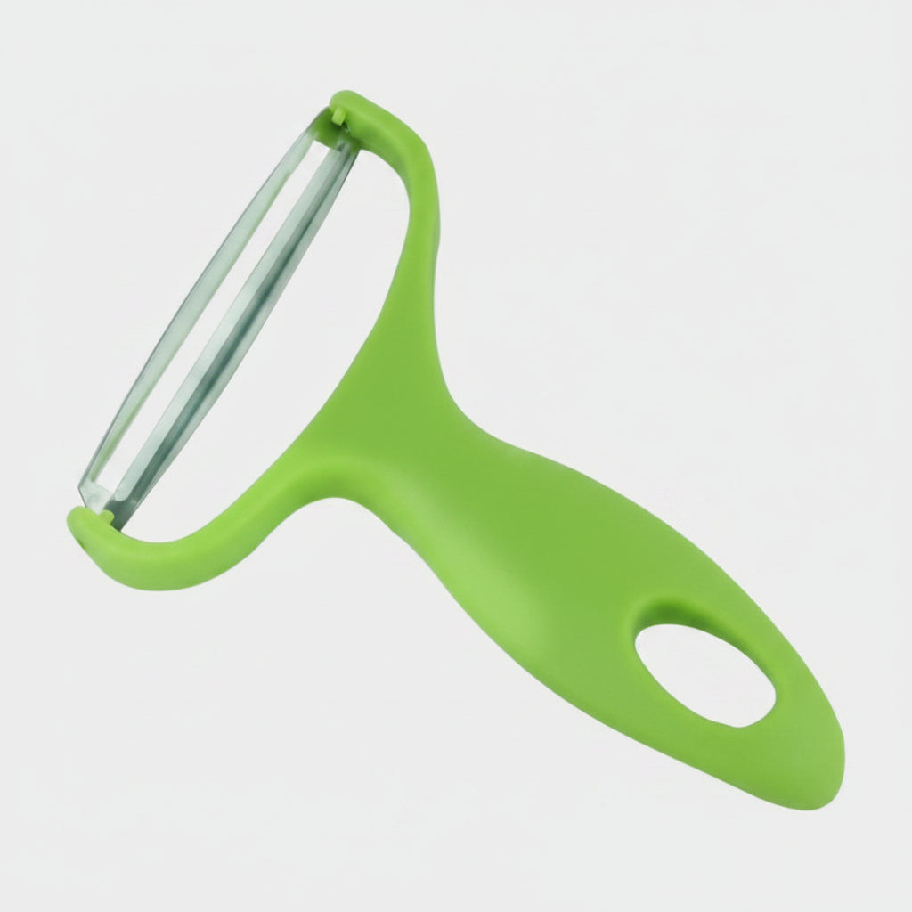 A green handheld vegetable peeler with a clear glass blade, shown over a yellow banner with fresh tomatoes, basil, and garlic against a blurred kitchen background.