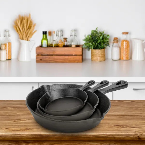 Set of three black cast iron skillets on a wooden kitchen counter with a white background.